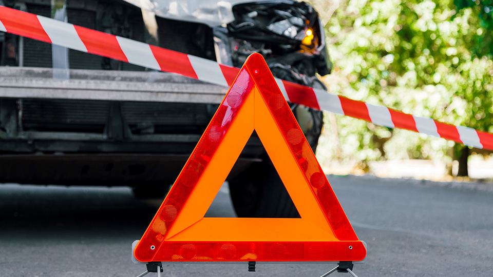 Warndreieck im Vordergrund und beschädigtes Auto im Hintergrund.