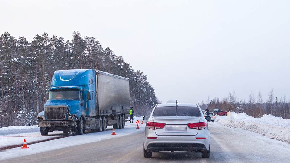 Fahrbahn mit Schnee bedeckt und überall stehen Warndreiecke. Ein blauer LKW und ein grauer PKW sind im Bild zu sehen.