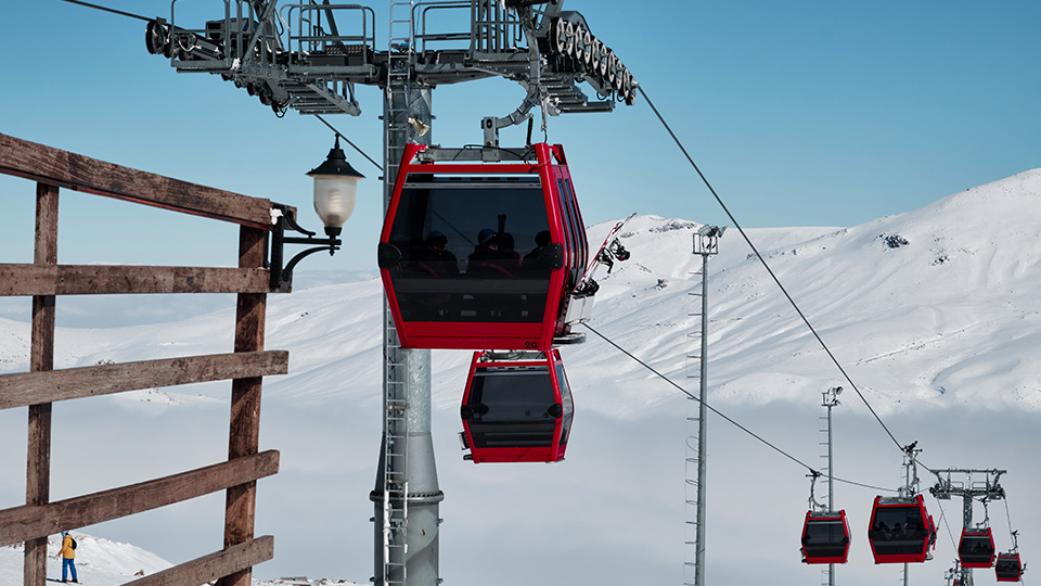 Mehrere rote Gondeln fahren eine Skipiste nach oben.