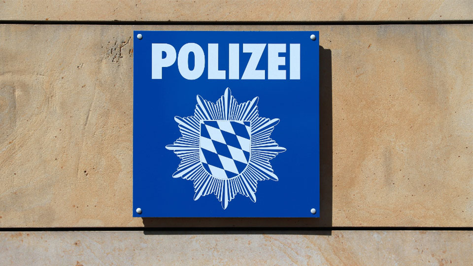 Polizei Schild in Blau-Weiß, das an einer beigen Wand hängt.