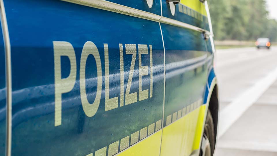 Streifenwagen der Polizei, der gerade am Fahrbahnrand steht, von der Seite: Schriftzug POLIZEI im Vordergrund.