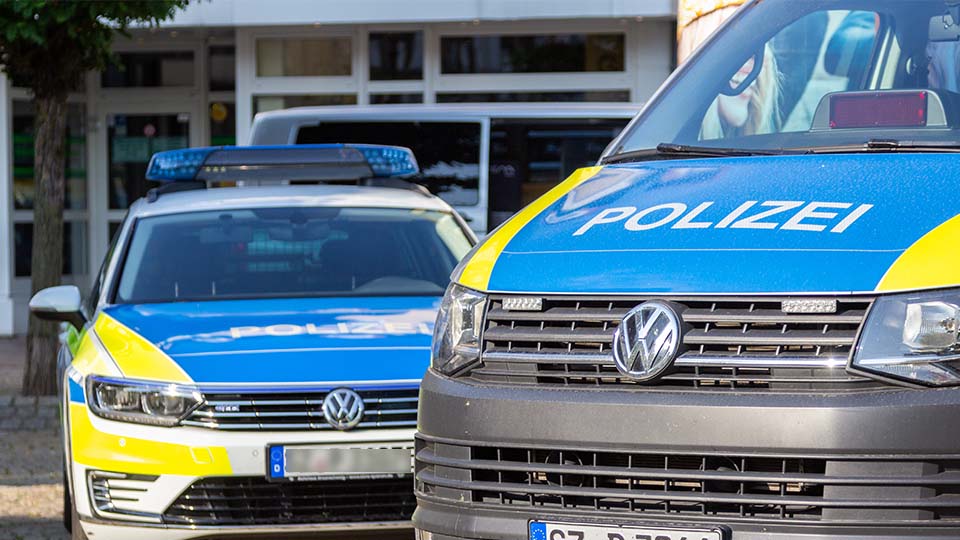 Zwei Streifenwägen der Polizei stehen schräg hintereinander vor einem Gebäude.