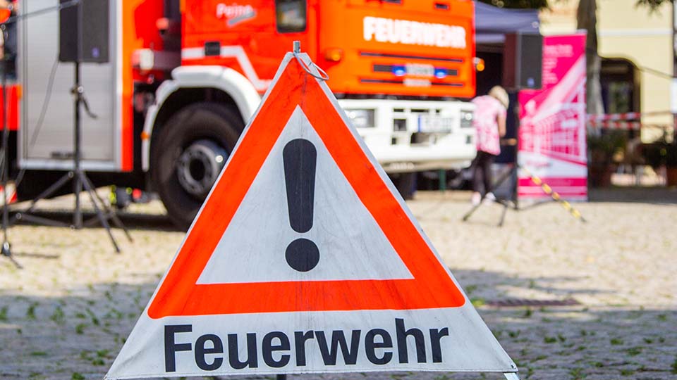 Warndreieck der Feuerwehr im Vordergrund und im Hintergrund ein Feuerwehrauto.