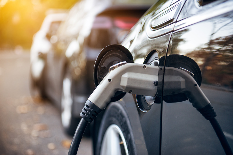 Electric car charging on parking lot with electric car charging station on city street. Electric cars in the row ready for charge. Close up of the power supply plugged into an electric car being charged.