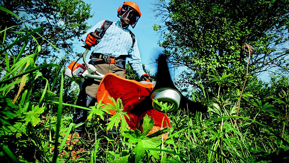 Mann mit orange-farbenem Helm verrichtet Gartenarbeit