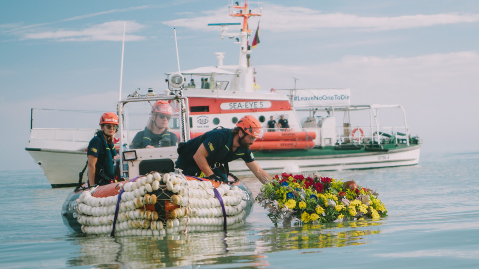 Menschen legen Blumenkranz ins Wasser, um den Toten zu gedenken