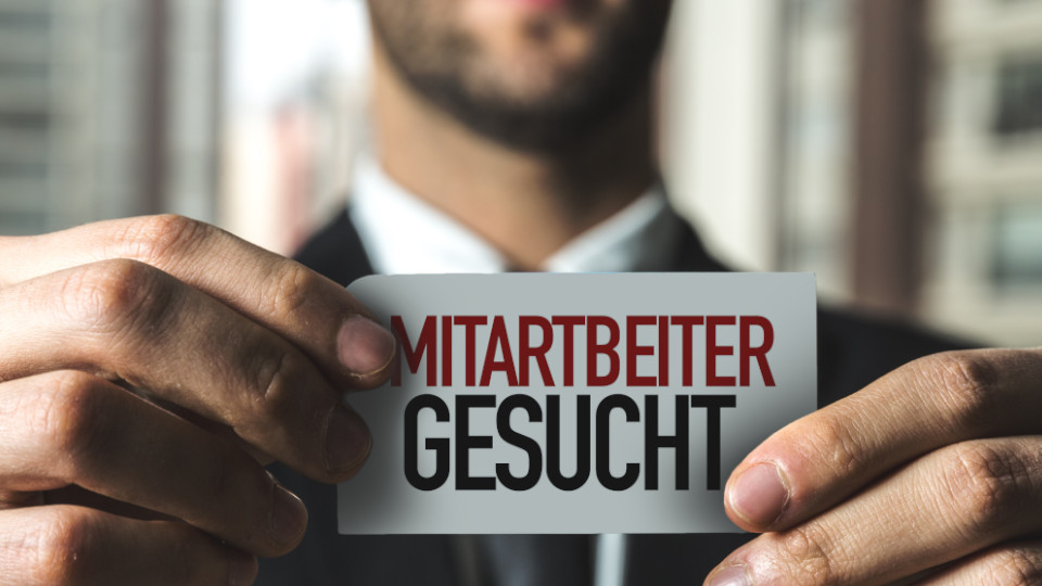 Mann hält ein Schild mit "Mitarbeiter gesucht"